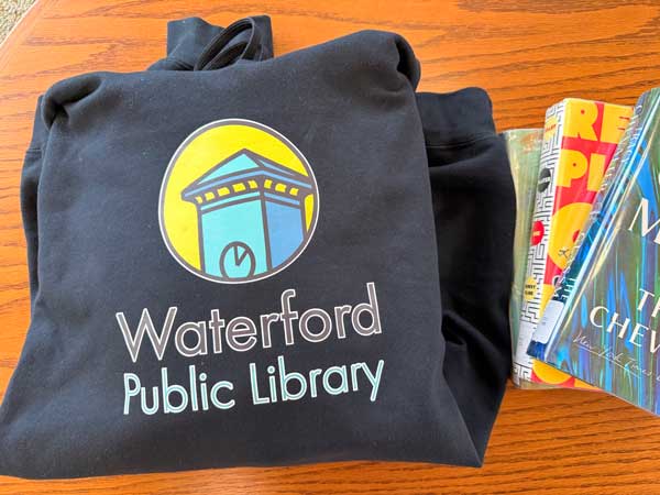 Waterford Public Library Hoodie with Logo Folded on Library Table with Books